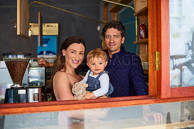 Buy stock photo Portrait of a smiling couple and their little girl standing at the window of their bakery