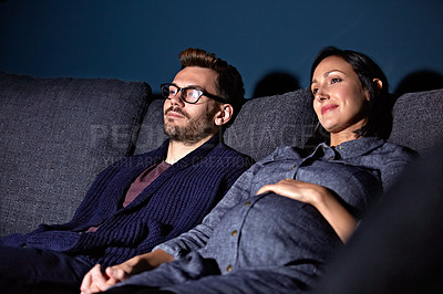 Buy stock photo Shot of a pregnant woman and her husband sitting on the sofa watching television in the evening
