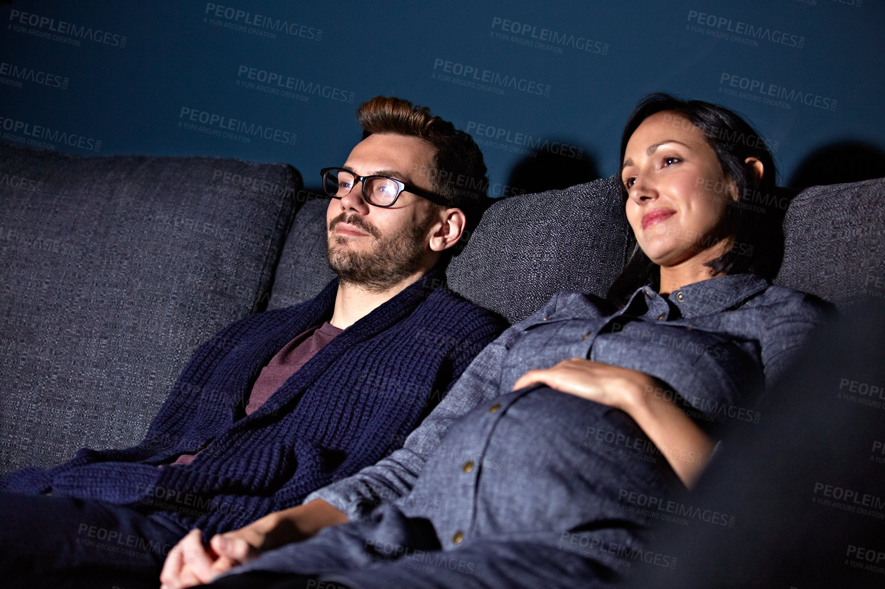 Buy stock photo Shot of a pregnant woman and her husband sitting on the sofa watching television in the evening
