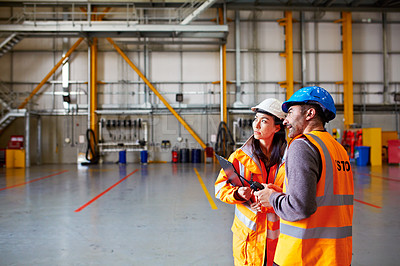 Buy stock photo Shot of two warehouse workers talking together inside of a large warehouse