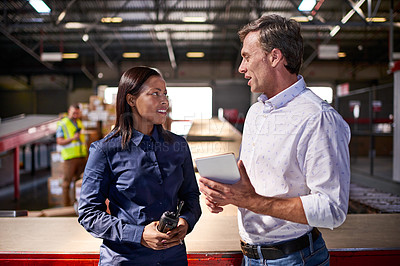 Buy stock photo Shot of two colleagues talking over a digital tablet while standing in a large warehouse