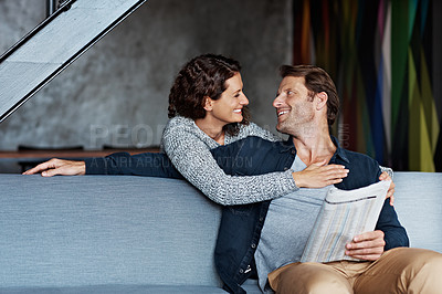 Buy stock photo Shot of a smiling woman hugging her husband from behind while sitting on a sofa in their living room