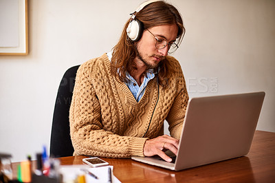 Buy stock photo Shot of a young designer working on a laptop and listening to music on headphones in an office