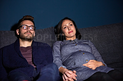 Buy stock photo Shot of a pregnant woman and her husband sitting on the sofa watching television in the evening