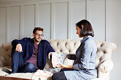 Buy stock photo Shot of a young pregnant woman showing her husband baby clothes on their sofa