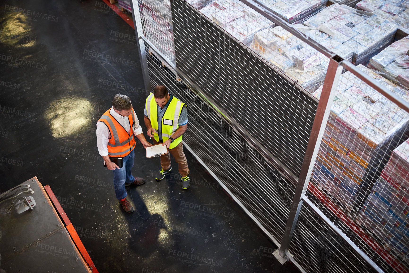 Buy stock photo High angle shot of two warehouse workers standing in a large warehouse