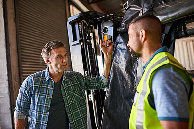 Buy stock photo Shot of two coworkers talking together by a florklift inside a large warehouse