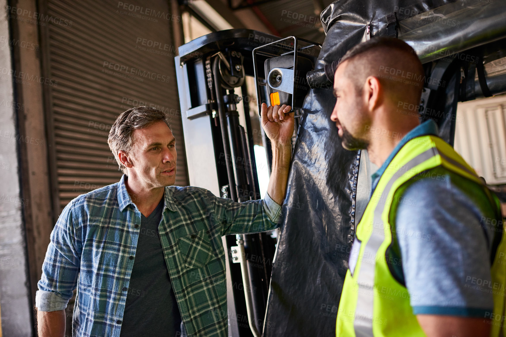 Buy stock photo Shot of two coworkers talking together by a florklift inside a large warehouse