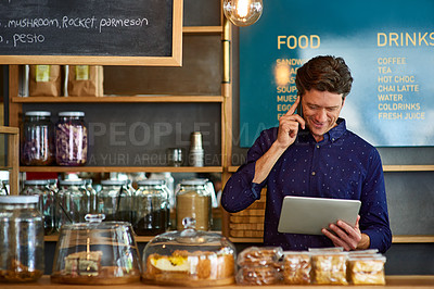 Buy stock photo Shot of a man talking on the phone and using a digital tablet while standing behind a counter in a cafe