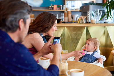 Buy stock photo Shot of a father taking a picture of his wife and baby girl while sitting in a cafe