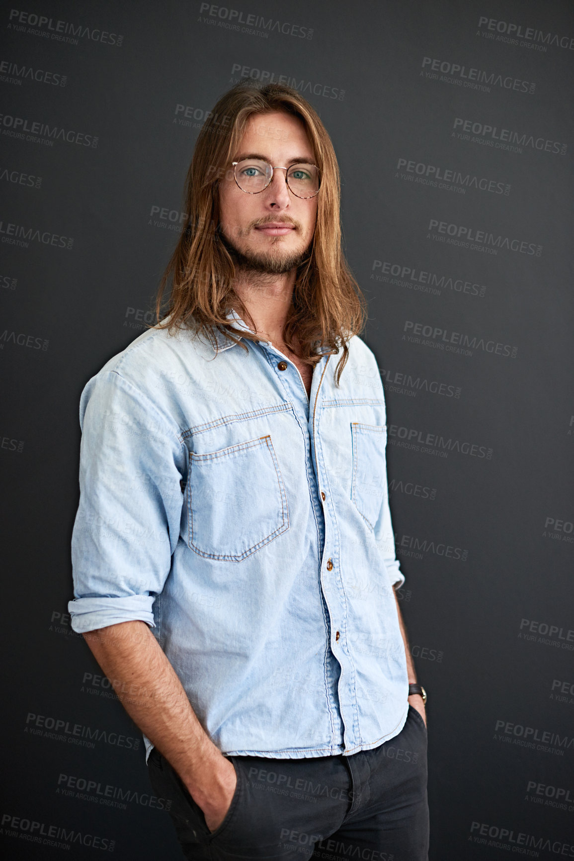 Buy stock photo Studio portrait of a young man standing with his hands in his pockets against a gray background