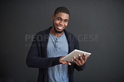 Buy stock photo Studio portrait of a smiling young man using a digital tablet against a gray background