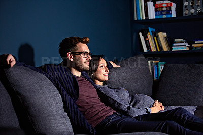 Buy stock photo Shot of a pregnant woman and her husband sitting on the sofa watching television in the evening