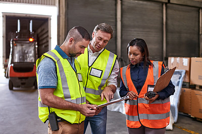 Buy stock photo Shot of a group of coworkers reading paperwork while standing in a large warehouse