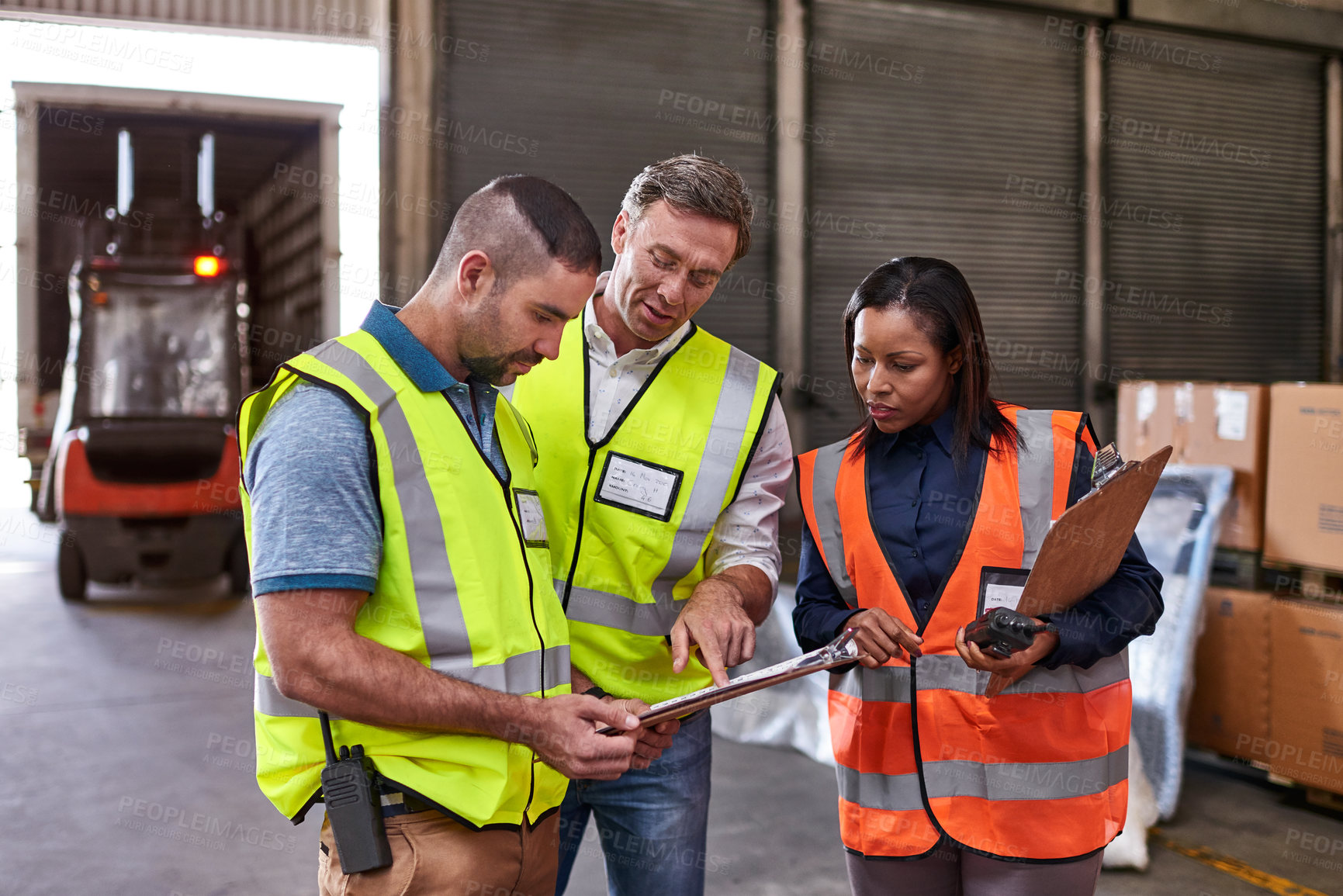 Buy stock photo Shot of a group of coworkers reading paperwork while standing in a large warehouse