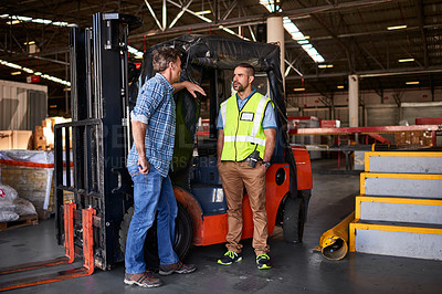 Buy stock photo Shot of two coworkers talking together by a florklift inside a large warehouse