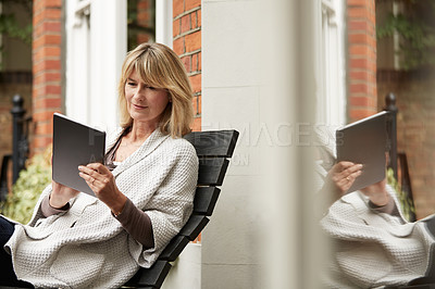 Buy stock photo Shot of a mature woman sitting on bench outside using a digital tablet