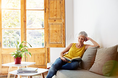 Buy stock photo Shot of a mature woman sitting on her sofa at home reading a book