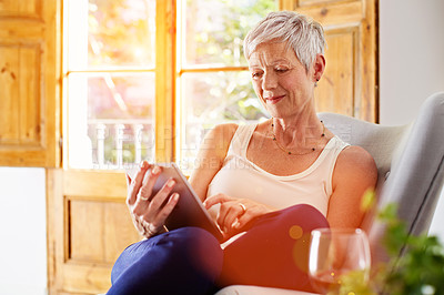 Buy stock photo Shot of a mature woman sitting in her living room using a digital tablet