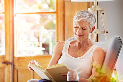Buy stock photo Shot of a mature woman relaxing on her sofa at home reading a book