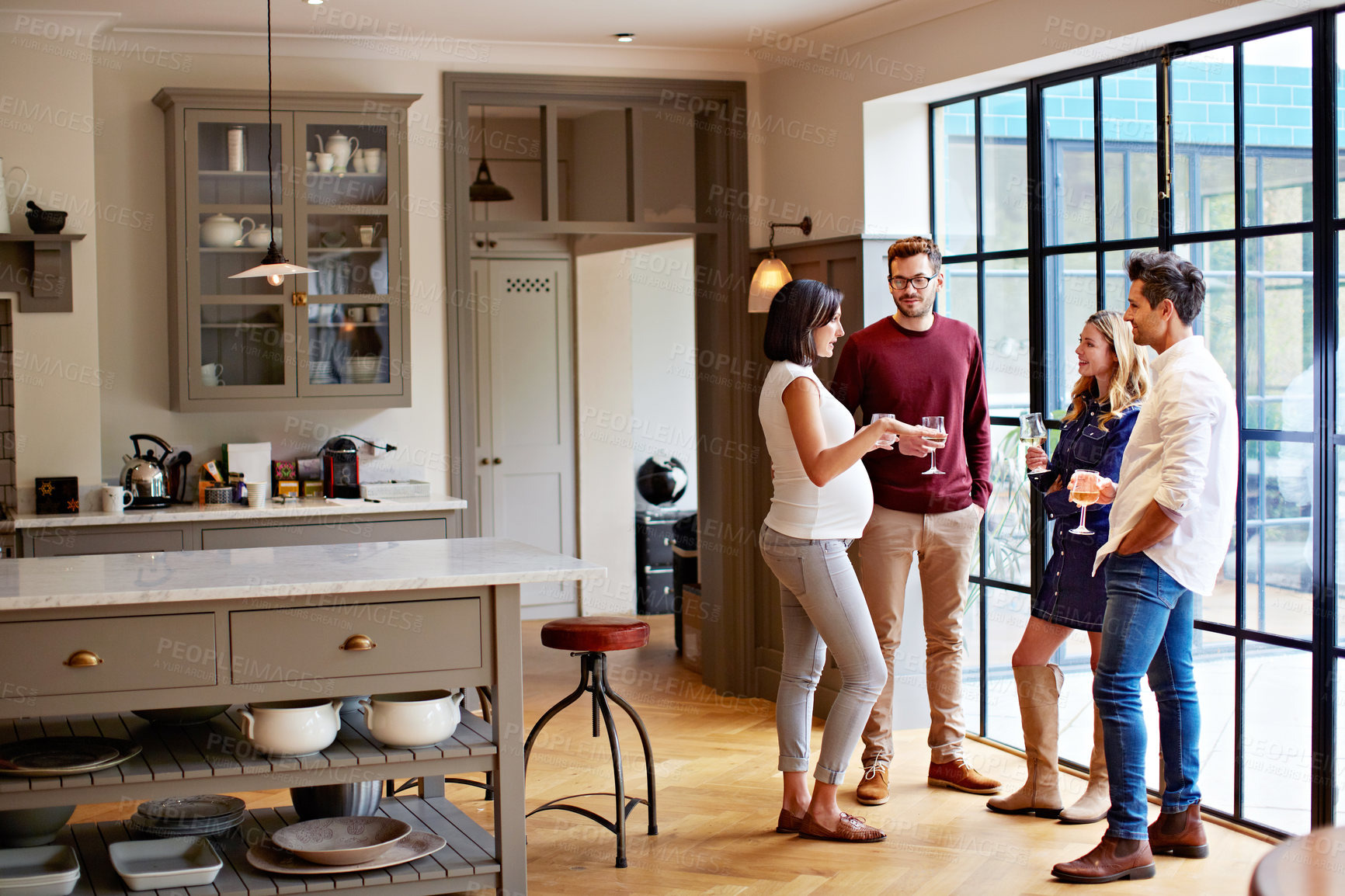 Buy stock photo Shot of a group of friends drinking wine and talking together in a kitchen at a get-together