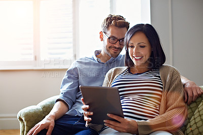 Buy stock photo Shot of a pregnant woman and her husband sitting on thier sofa using a digital tablet