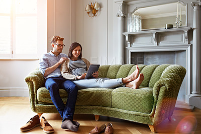 Buy stock photo Shot of a pregnant woman and her husband sitting on thier sofa using a digital tablet