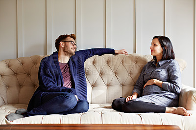 Buy stock photo Shot of a young expecting couple talking together while sitting on the sofa at home