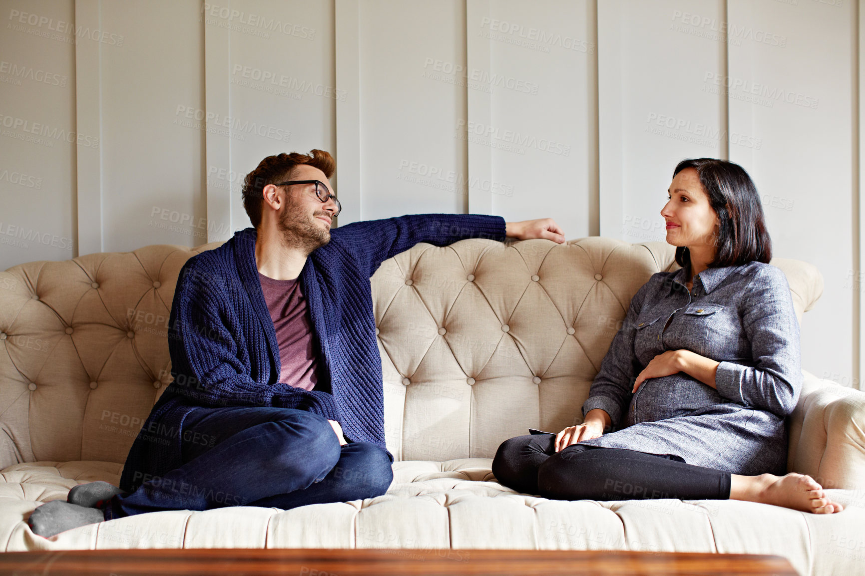Buy stock photo Shot of a young expecting couple talking together while sitting on the sofa at home
