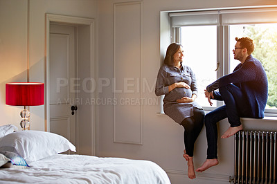 Buy stock photo Shot of a young pregnant woman talking with her husband while sitting on a window sill at home