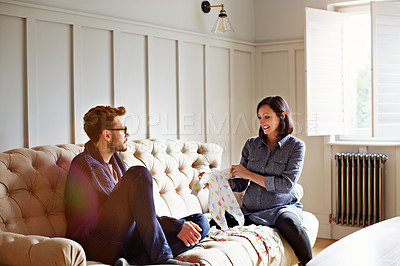 Buy stock photo Shot of a young pregnant woman showing her husband baby clothing while sitting on their sofa