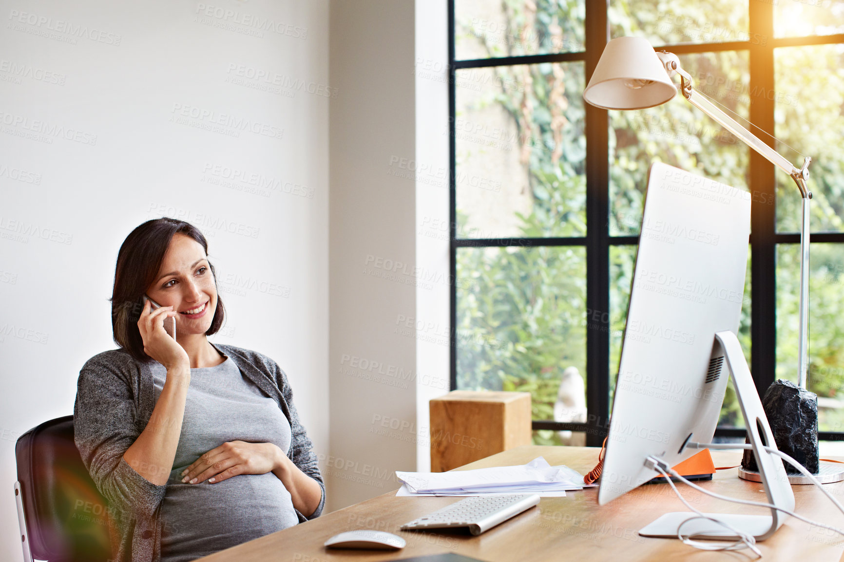 Buy stock photo Shot of a pregnant woman talking on the phone while sitting at a desk in her home office