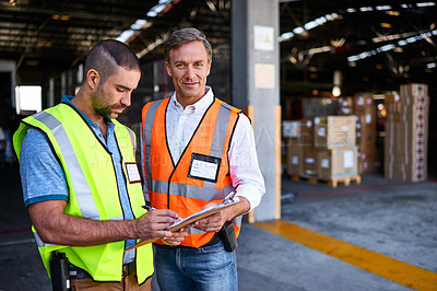 Buy stock photo Shot of two workers talking together over a clipboard while standing at the entrance of a warehouse