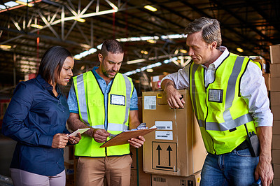 Buy stock photo Shot of a group of coworkers reading paperwork while standing in a large warehouse