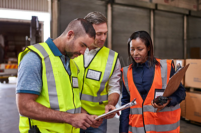 Buy stock photo Shot of a group of coworkers reading paperwork while standing in a large warehouse