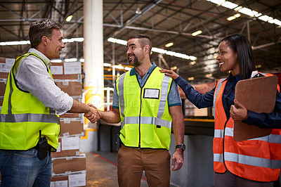 Buy stock photo Shot of two workers shaking hands together in a large warehouse while a coworker looks on