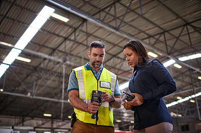 Buy stock photo Shot of two coworkers looking at a barcode reader while standing in a large warehouse