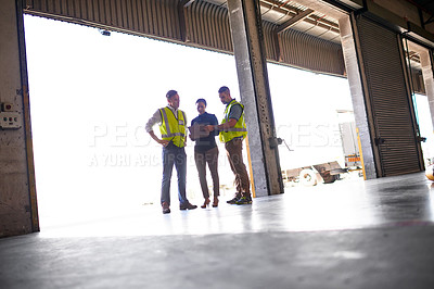 Buy stock photo Shot of three workers talking together inside the entrance to a large warehouse