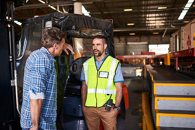 Buy stock photo Shot of two coworkers talking together beside a forklift while standing in a large warehouse