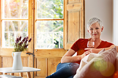 Buy stock photo Portrait of a smiling mature woman relaxing on a sofa at home with a glass of wine
