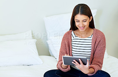 Buy stock photo Shot of a young woman sitting on her bed using a digital tablet