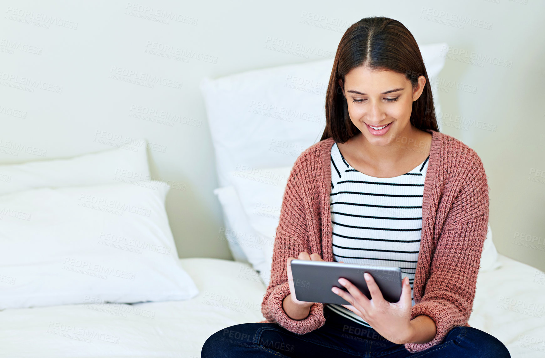 Buy stock photo Shot of a young woman sitting on her bed using a digital tablet