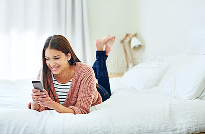Buy stock photo Shot of a young woman lying on her bed using a cellphone
