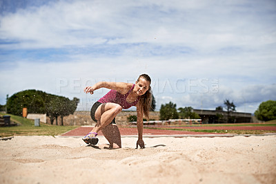 Buy stock photo Shot of a young woman landing in sand after a long jump