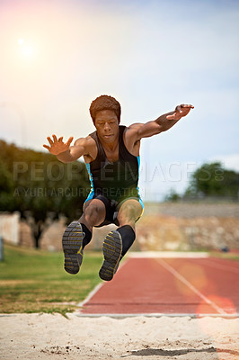 Buy stock photo Shot of a young woman in mid air doing a long jump on a sports field