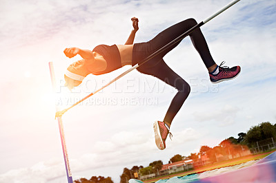 Buy stock photo Shot of a young woman in mid air doing a high jump on a sports field