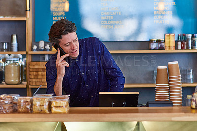 Buy stock photo Shot of a man talking on the phone while standing behind a counter in a cafe