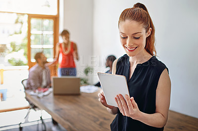 Buy stock photo Shot of a smiling young woman using a digital tablet in an office with colleagues in the background