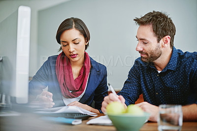 Buy stock photo Shot of two colleagues comparing paperwork while sitting at a desk in an office