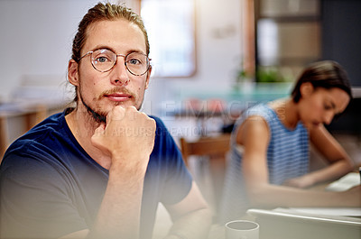 Buy stock photo Portrait of a focused young designer sitting in an office with a colleauge in the background